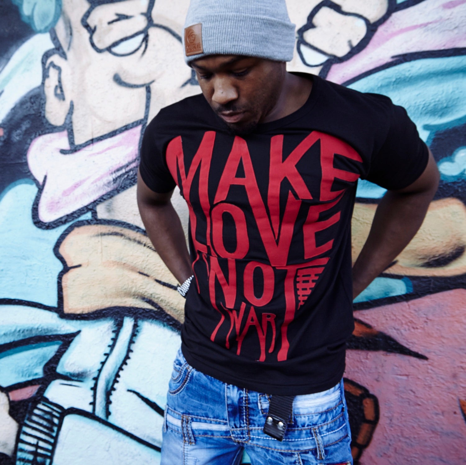 Manchester's Fullahype in a Custom Appliqued T-shirt, Blood red make love not war textile logo, cut and sewed onto a earth positive Black organic cotton heavyweight T-shirt. Graffiti wall at the side of the shop Ridelow in the background. 